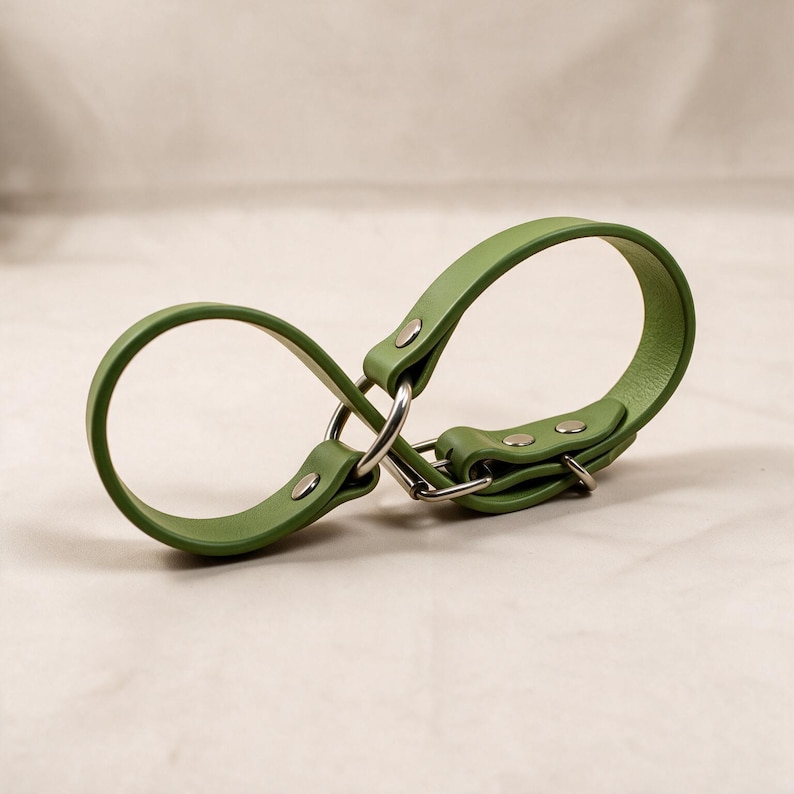 A green leather strap with metal buckles and clips is shown against a light background.