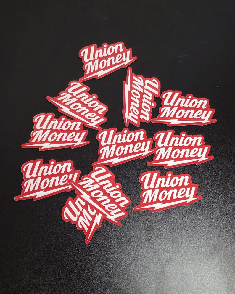 May include: A collection of red and white stickers with the words "Union Money" in a stylized font. The stickers have a lightning bolt design element and are scattered on a dark surface.