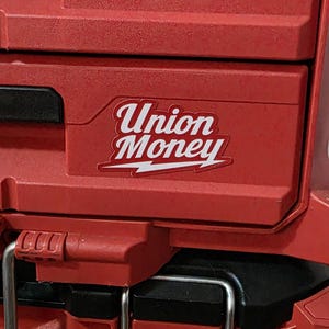 May include: Red tool box with the words "Union Money" in white script on a sticker. The sticker has a white lightning bolt design. The tool box has a black handle and metal latches.