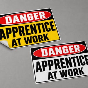 May include: Two rectangular safety signs featuring a red oval with the white text DANGER at the top. Below, the text APPRENTICE AT WORK is printed in bold black letters. One sign has a yellow background, while the other has a white background.