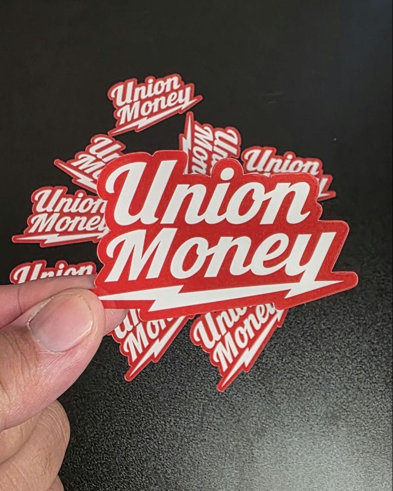 May include: A collection of red and white stickers with the words "Union Money" in a bold, stylized font. The stickers have a lightning bolt design element and are scattered on a dark surface.