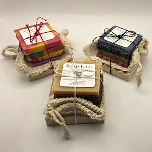 Puede incluir: Tres montones de coloridos restos de jabón, cada uno atado con hilo y una etiqueta, descansan en bolsas de malla beige. Los jabones están en un soporte de madera. Las etiquetas dicen "Soap Ends Tester Pack".