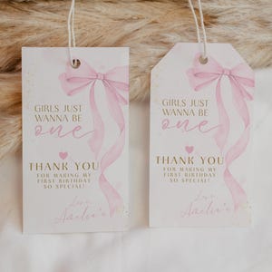 Puede incluir: Dos etiquetas de regalo blancas con lazos y cintas rosas de acuarela. Las etiquetas dicen "GIRLS JUST WANNA BE ONE" y "THANK YOU FOR MAKING MY FIRST BIRTHDAY SO SPECIAL!" con un corazón y el nombre "Amelia's".