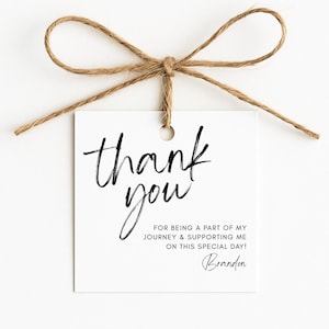 Pode incluir: Uma etiqueta quadrada de papel branco com um furo no topo, amarrada com um laço de barbante marrom. A etiqueta apresenta o texto preto thank you, seguido por FOR BEING A PART OF MY JOURNEY & SUPPORTING ME ON THIS SPECIAL DAY! e o nome Brandon.