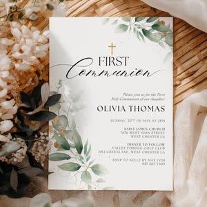 Può includere: Un invito per la Prima Comunione con calligrafia elegante e una croce dorata. L'invito presenta il testo "First Communion" e i dettagli dell'evento di Olivia Thomas, accentuato da foglie verdi e dettagli dorati.