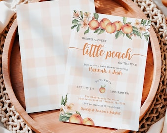 May include: A baby shower invitation with a peach theme. The invitation features the text "There's a sweet little peach on the way!" and includes the names Hannah & Josh. The invitation is on a wooden tray with a peach gingham envelope.