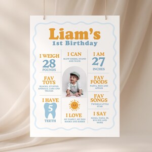 Może przedstawiać: Spersonalizowany plakat na pierwsze urodziny, z imieniem "Liam's" w kolorze pomarańczowym. Plakat zawiera szczegóły takie jak waga (12,7 kg), wzrost (68,6 cm), ulubione zabawki, jedzenie i piosenki, wraz ze zdjęciem dziecka.