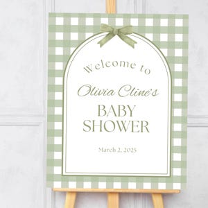 May include: A green and white gingham welcome sign with a green bow and the text "Welcome to Olivia Cline's Baby Shower March 2, 2025"