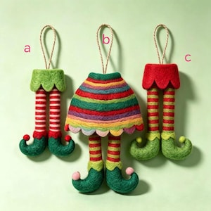 May include: Three felt hanging ornaments labeled a, b, and c. Ornament a features green elf legs with red and white stripes. Ornament b shows a striped skirt with green and red legs. Ornament c displays red elf legs with green and red stripes.