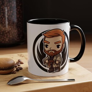 May include: White ceramic mug with a black rim and handle. The mug features a cartoon illustration of a red-haired man with a beard, wearing a brown and white robe. The illustration is surrounded by a black and white circle design.