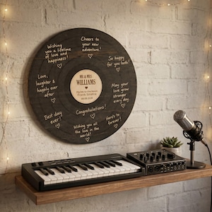 Könnte beinhalten: Eine hölzerne Hochzeitsplatte mit graviertem Text und Herzen, personalisiert mit den Namen und dem Hochzeitsdatum eines Paares. Eine Tastatur, ein Audio-Interface und ein Mikrofon stehen auf einem Holzregal darunter.