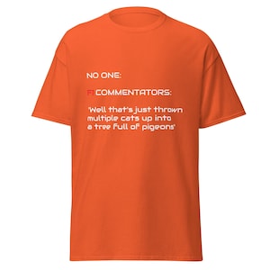 May include: Orange t-shirt with the text "NO ONE: FI COMMENTATORS: 'Well that's just thrown multiple cats up into a tree full of pigeons'". The shirt has a crew neck and short sleeves.