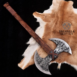 May include: A double-bladed axe with a wooden handle and a textured metal blade. The handle is wrapped with brown leather. The axe is lying on a brown and white animal hide. The axe is a handcrafted item.