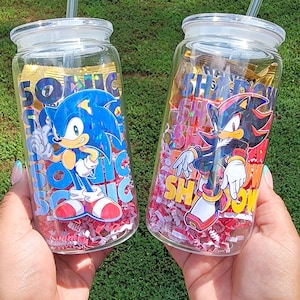 May include: Two clear glass tumblers with lids and straws, each featuring a different Sonic the Hedgehog character. One tumbler has Sonic, the other has Shadow. Both are filled with red and white confetti.