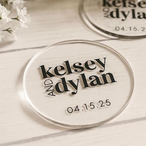 Op de afbeelding: Transparante acryl onderzetters met de namen "Kelsey" en "Dylan" in zwarte letters, en de datum "04.15.25". De ronde onderzetters zijn helder en geschikt voor gepersonaliseerde huwelijksbedankjes of cadeaus.