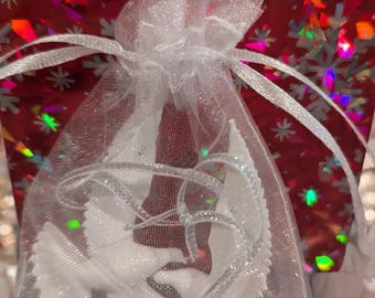 Puede incluir: Una bolsa de organza blanca transparente con una cinta de satén blanca atada alrededor de la parte superior. La bolsa está llena de palomas blancas, que son una decoración navideña popular.