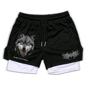 May include: Black athletic shorts with a white inner layer, featuring a wolf graphic on the left leg, the text "Breathe. Focus. Conquer" below it, and stylized white text on the right leg. The shorts have an elastic waistband with black drawstrings.