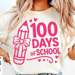 以下が含まれることがあります： 100日間の学校を祝うピンク色のグラフィックが特徴のクリーム色のTシャツ。デザインには、リボン付きの鉛筆、「100 DAYS of SCHOOL」の文字、小さなハートが含まれています。デジタルダウンロードオプションがリストされています。