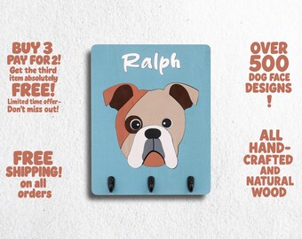 May include: A blue wooden key holder with three hooks and a bulldog face cutout. The dog's name, "Ralph", is written above the dog. The text "Over 500 Dog Face Designs!" is in the upper right corner. The text "All Hand-Crafted and Natural Wood" is in the lower right corner.
