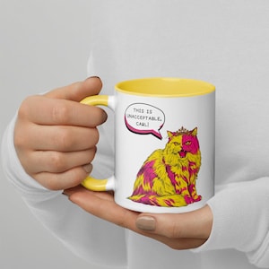以下が含まれることがあります： 黄色い内側とハンドルが付いた白いセラミックマグ。マグカップには、王冠をかぶった黄色とピンクの漫画の猫のイラストと、「THIS IS UNACCEPTABLE, CARL!」と書かれた吹き出しが付いています。
