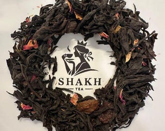 May include: Close-up of loose leaf tea with dried petals and fruit. The tea is arranged around a white circle with the text "SHAKH TEA" and a silhouette of a woman drinking tea.