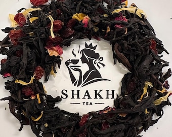 May include: Close-up of loose leaf tea with dried berries and flower petals. The tea is arranged around a white circle with a black and white logo that reads "SHAKH TEA". The logo features a silhouette of a woman drinking tea.