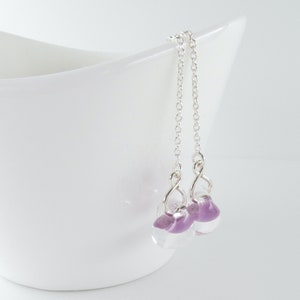 May include: A pair of silver dangle earrings with small, clear glass beads that have a purple hue.
