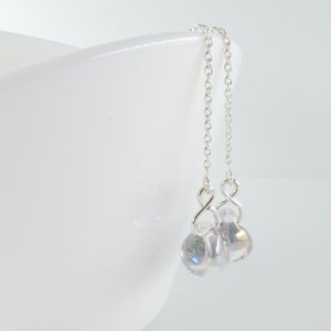 Peut inclure: Boucles d'oreilles pendantes en argent avec des perles de verre irisées. Les perles sont rondes et ont une finition nacrée.