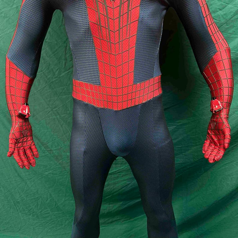 May include: A full-body spandex suit featuring a dark blue textured base with a red chest panel and red sleeves, both overlaid with a black web pattern. The suit includes red gloves with black webbing and small red mechanical wrist attachments.