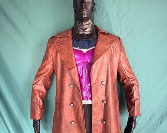 May include: A brown, double-breasted trench coat with a textured appearance. The coat is worn over a purple and blue costume. The mannequin also wears a black head covering and gloves. The coat has large lapels and several buttons.