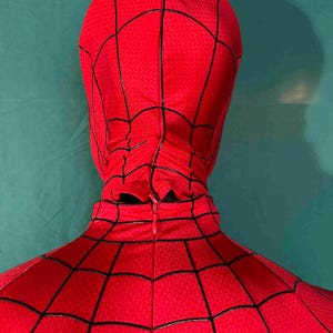Puede incluir: Disfraz de Spider-Man rojo y negro, con un patr&oacute;n texturizado y detalles de telara&ntilde;a negros. El disfraz incluye una capucha y una cremallera en la espalda. El dise&ntilde;o general es rojo vibrante con l&iacute;neas negras.