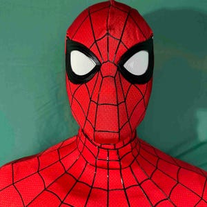 Puede incluir: Una m&aacute;scara de Spider-Man roja y negra con lentes oculares blancas. La m&aacute;scara presenta un patr&oacute;n de telara&ntilde;a y est&aacute; hecha de un material texturizado. La imagen es un primer plano, que muestra los detalles del dise&ntilde;o.