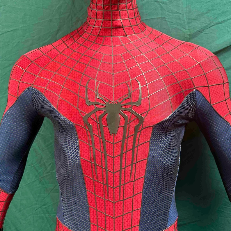 May include: A full-body spandex suit featuring a vibrant red chest and shoulder section with a black web pattern and a large black spider emblem in the center. The sides and arms are a textured dark blue material with a honeycomb-like pattern.