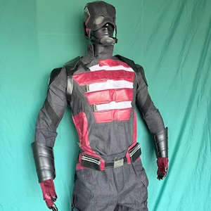 May include: A full costume displayed on a mannequin. The outfit is mainly grey with red and white details. It features a helmet, chest piece, arm guards, gloves, and trousers. The helmet is black with a visor. The chest piece has red and white stripes.