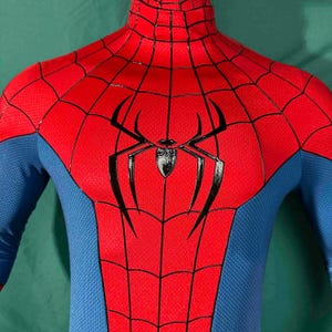 Puede incluir: Un disfraz de Spider-Man rojo y azul. Las secciones rojas presentan un patr&oacute;n de telara&ntilde;a y el emblema de la ara&ntilde;a negra est&aacute; centrado en el pecho. Las secciones azules est&aacute;n en los brazos y los lados. El disfraz tiene un cuello alto.