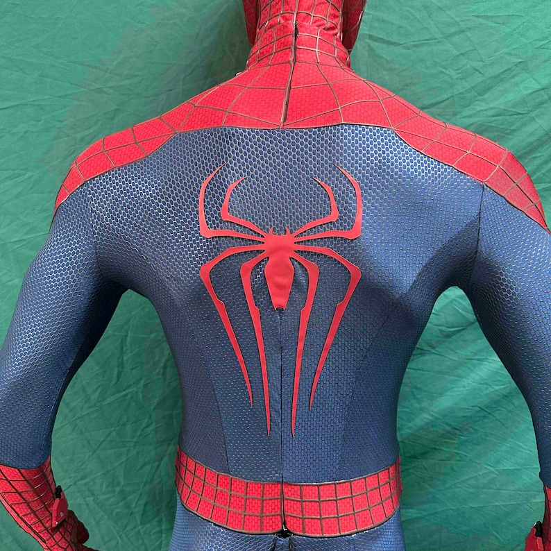 May include: A full-body spandex costume featuring a textured blue base with red sections on the shoulders and waist. A large, elongated red spider emblem is centered on the back, complemented by a black web pattern printed over the red areas.