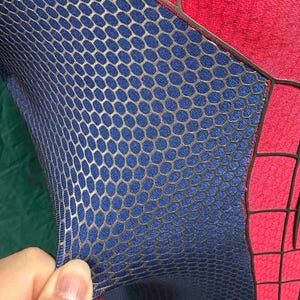 May include: A stretchable fabric garment featuring a blue section with a raised, metallic silver honeycomb pattern and a red section with a black grid design. The material is flexible and textured, showing a distinct contrast between the two colors.