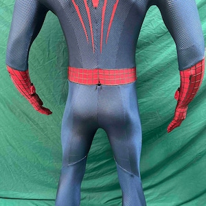 May include: A full-body spandex suit featuring a dark blue base with a textured honeycomb pattern. The design includes red accents on the forearms and a red waist belt with a black grid pattern. Red vertical lines extend upward from the waist.