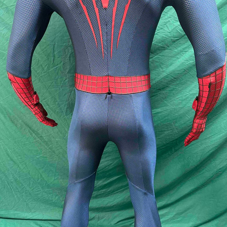 May include: A full-body spandex suit featuring a dark blue base with a textured honeycomb pattern. The design includes red accents on the forearms and a red waist belt with a black grid pattern. Red vertical lines extend upward from the waist.