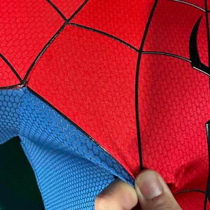 Puede incluir: Primer plano de un disfraz de superh&eacute;roe rojo y azul. Las secciones rojas tienen un patr&oacute;n texturizado, con l&iacute;neas negras que delinean el dise&ntilde;o. La secci&oacute;n azul tiene un patr&oacute;n de panal.