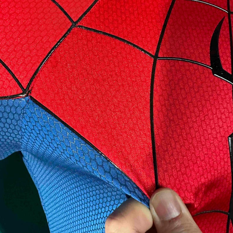 Puede incluir: Primer plano de un disfraz de superh&eacute;roe rojo y azul. Las secciones rojas tienen un patr&oacute;n texturizado, con l&iacute;neas negras que delinean el dise&ntilde;o. La secci&oacute;n azul tiene un patr&oacute;n de panal.