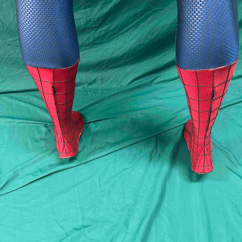 May include: A pair of costume leggings featuring a blue upper section with a textured honeycomb pattern and a red lower section with a black webbed grid design. The red portions extend from the mid-calf down to the feet and include a vertical zipper.