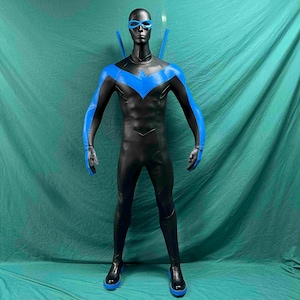 May include: A full-body superhero costume featuring a black bodysuit with a prominent blue bird-shaped emblem across the chest and shoulders. The outfit includes a matching blue domino mask and two blue sticks extending from behind the shoulders.