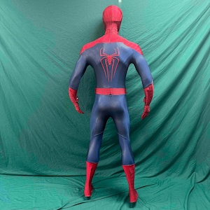 May include: A full-body spandex costume featuring a red and blue color scheme with a black web pattern. The back displays a large red spider emblem centered on the blue torso section, with red sleeves and leggings featuring a grid-like design.