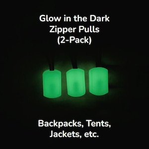 Puede incluir: Tres tiradores de cremallera verdes brillantes sobre cordones negros. La imagen incluye el texto "Glow in the Dark Zipper Pulls (2-Pack)" y "Backpacks, Tents, Jackets, etc."