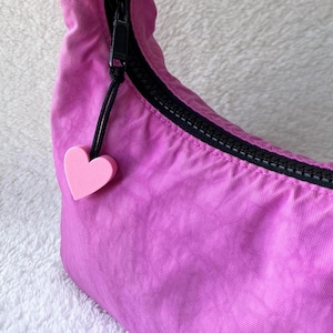 Puede incluir: Un bolso de nylon rosa con una cremallera negra y un charm de corazón rosa.