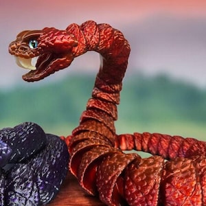 May include: Two detailed snake figurines. One is a deep red-brown with an open mouth, revealing white fangs. The other is a dark blue-purple with a coiled body. Both have detailed scales and vibrant, contrasting eye colours.