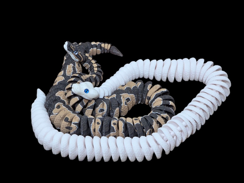 May include: A detailed sculpture of a rattlesnake with a coiled white tail. The snake's body is patterned with black, tan, and brown markings. It has a white head with blue eyes, set against a black background.