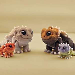 May include: Three small, hand-painted figurines of horned lizards. The lizards are in various poses and have different colored bodies, including brown, orange, and purple.