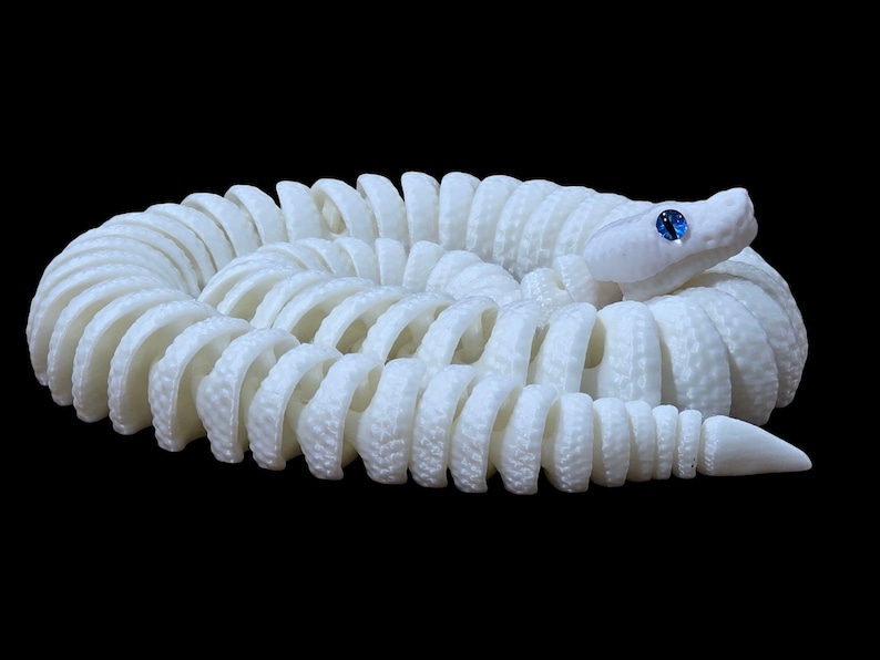 May include: A coiled white snake sculpture with a textured surface. The snake has a detailed design and a blue gem for an eye. The sculpture is set against a black background.